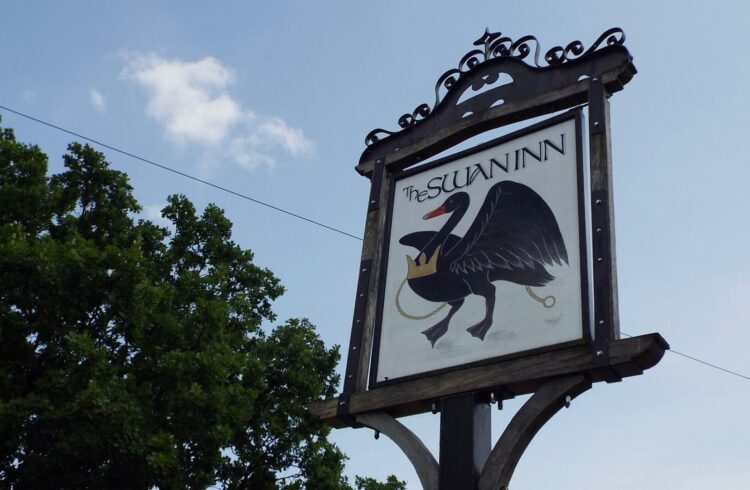 Pub sign at The Swan Inn with blue sky and tree behind